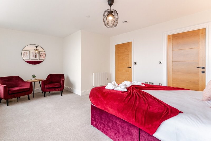 Spacious bedroom with double bed, red velvet bedding, burgundy armchairs, wooden doors and pendant light