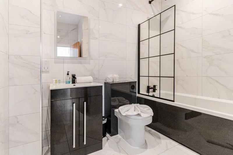 Modern bathroom with marble tile walls, black vanity, white toilet, and shower enclosure
