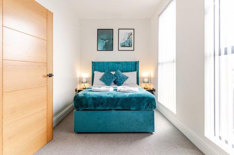 Modern bedroom with teal upholstered bed, white bedding, wooden door and bright windows