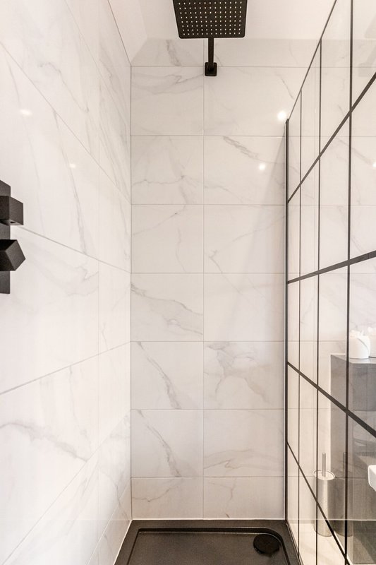 Modern bathroom shower enclosure with marble-effect wall tiles and black fixtures