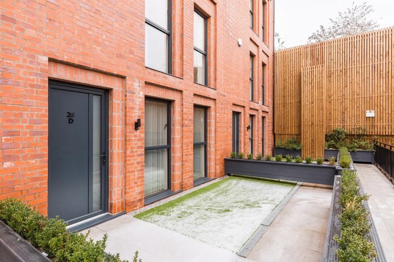 Modern brick building exterior with patio area, wooden fence, and landscaped garden