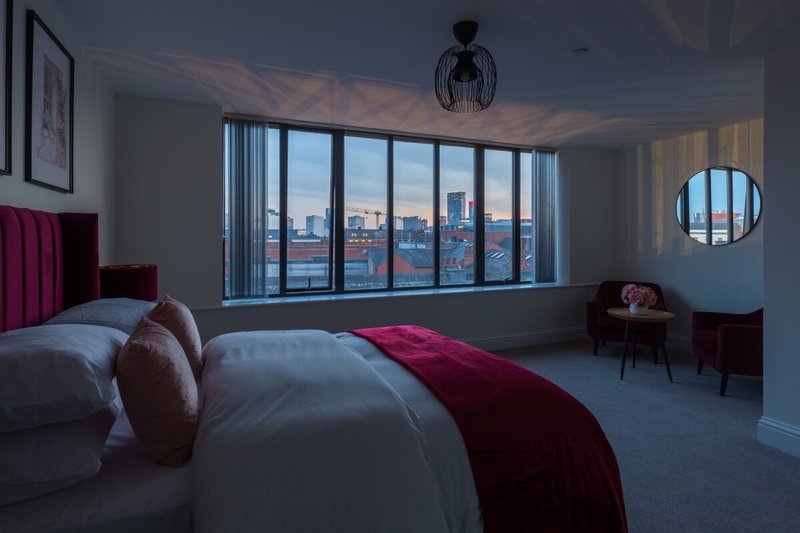 Modern bedroom with double bed, burgundy accents, city skyline views through large windows