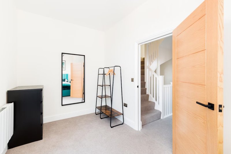 Bright modern bedroom with wooden door, mirror, ladder shelf and white radiator