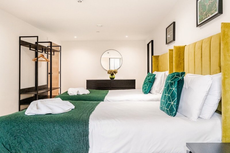 Modern bedroom with two beds, yellow headboards, green throws and white pillows