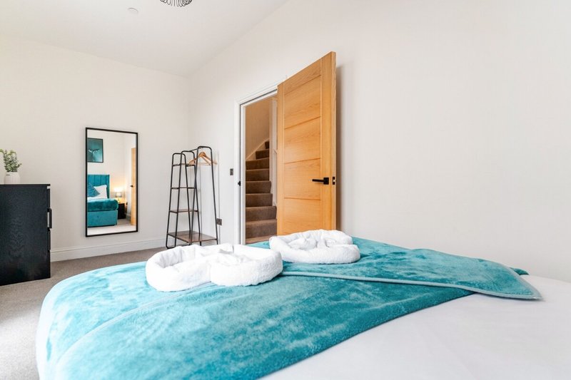 Bright bedroom with turquoise bed, white pillows, wooden door and framed mirror
