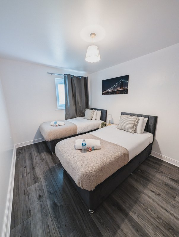 Modern bedroom with two single beds, dark wooden flooring and pendant ceiling light