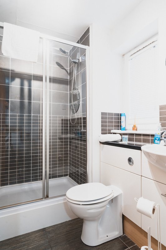 Clean modern bathroom with shower cubicle, toilet, sink and dark tile walls