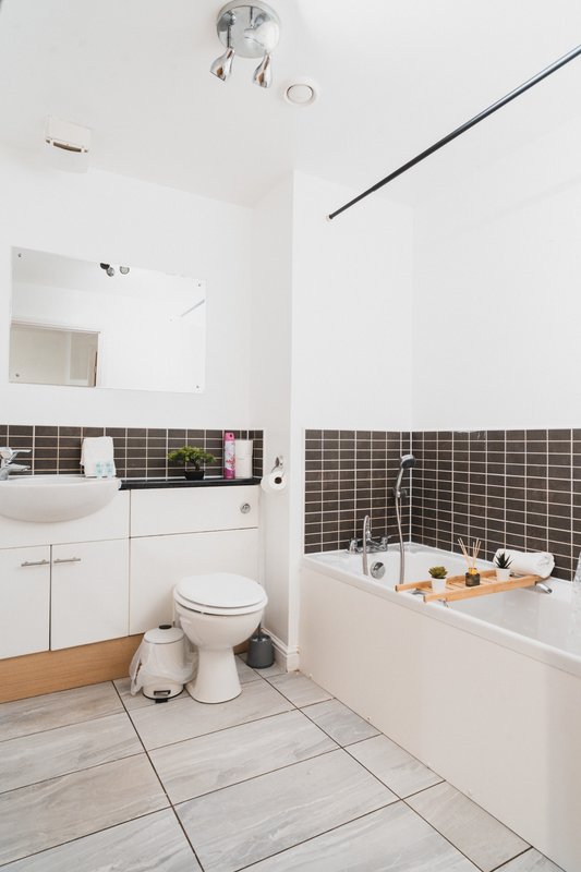Modern bathroom with white vanity, toilet, bathtub with dark tile surround and wooden floor