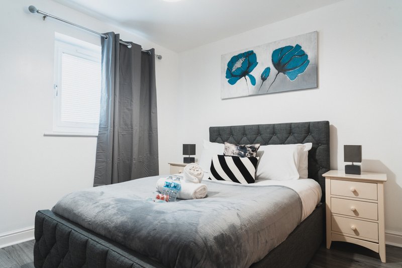 Modern bedroom with dark upholstered bed, white nightstand, teal abstract wall art
