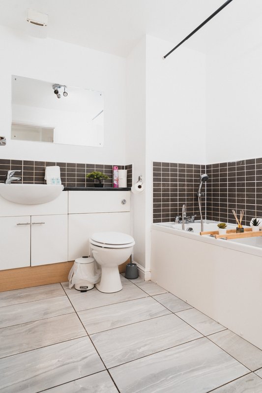 Modern bathroom with white sink, toilet, bathtub, black tile accents and wooden vanity