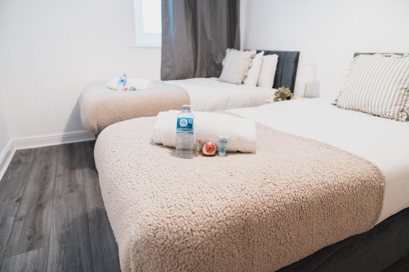 Modern bedroom with two single beds, cream bedding, dark wooden floor and neutral decor