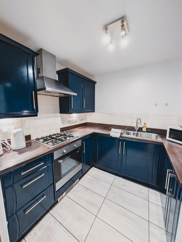 Modern kitchen with dark blue cabinets, gas hob, wooden countertops and white tile flooring