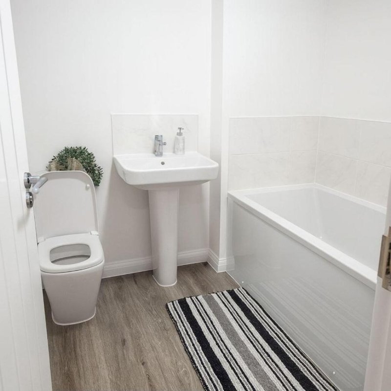 Clean white bathroom with toilet, pedestal sink, bathtub, and striped floor mat