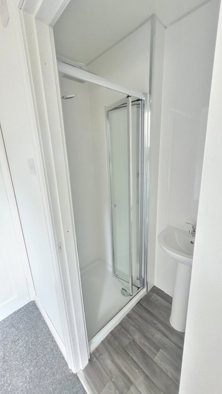 Compact bathroom with shower enclosure, toilet, and wood-effect vinyl flooring
