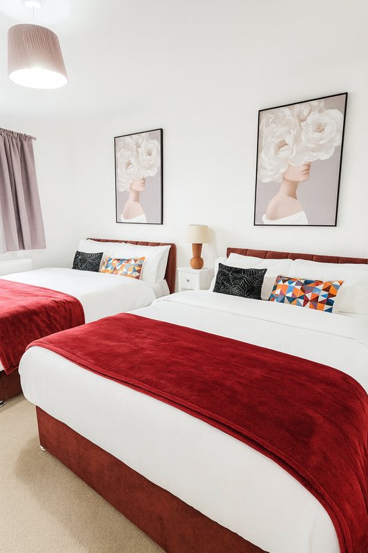 Twin bedroom with red bed runners, white bedding, framed wall art, and pendant lamp