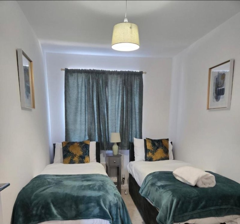 Twin bedroom with green bedspreads, patterned cushions, window with teal curtains and pendant light