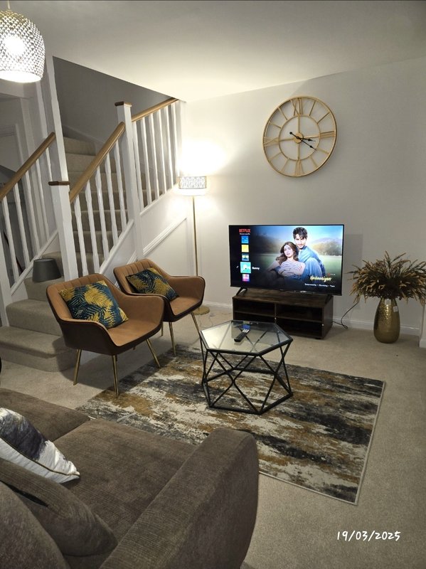 Modern living room with seating, TV, wooden clock, staircase and potted plant