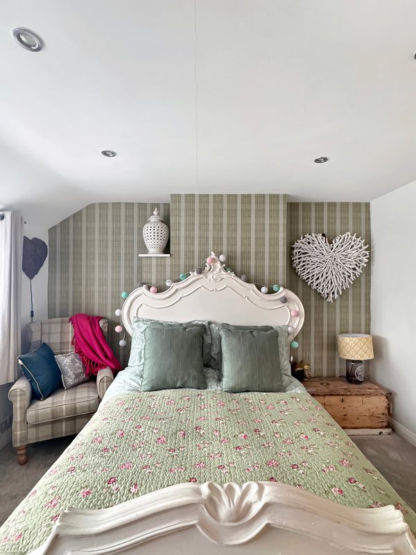 Bedroom with ornate white headboard, patterned bedding, striped wallpaper and decorative wall art