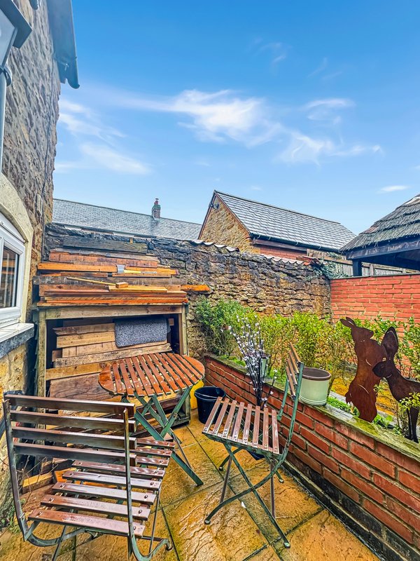 Outdoor patio area with wooden chairs, potted plants, and brick building walls