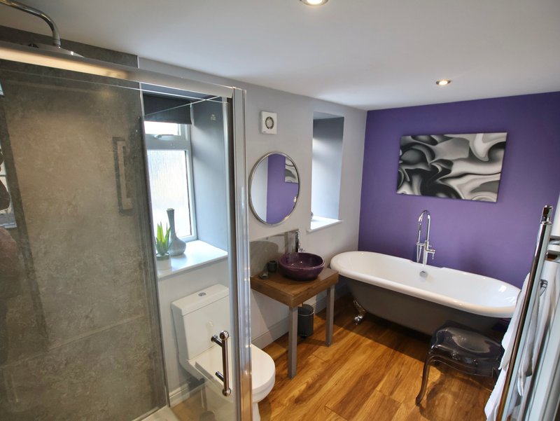Modern bathroom with purple accent wall, freestanding bathtub, walk-in shower, and wooden flooring