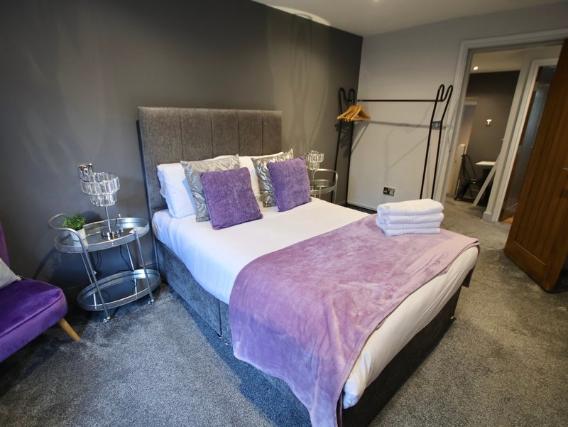 Modern bedroom with purple bedding, upholstered headboard, bedside table and wardrobe