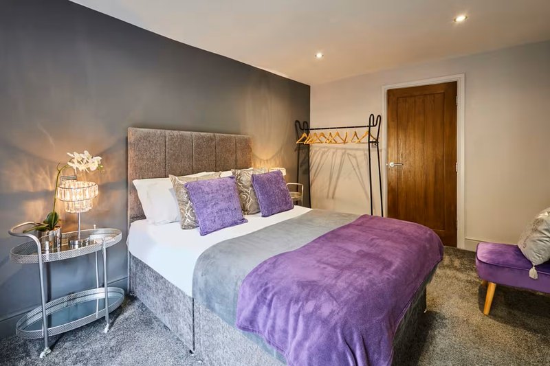 Modern bedroom with purple accents, double bed, bedside lamp and wooden door