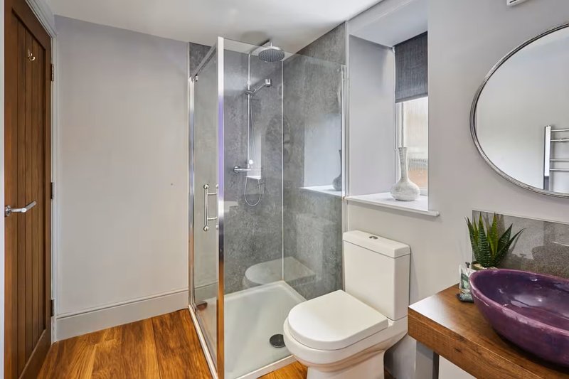 Modern bathroom with walk-in shower, toilet, wooden vanity, round mirror and window
