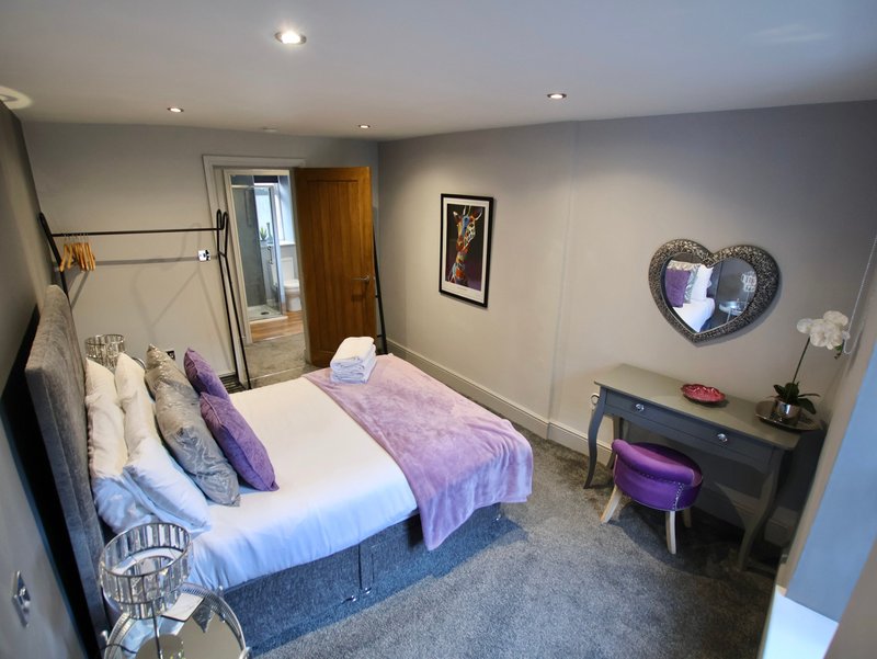 Modern bedroom with double bed, purple bedding, dressing table, and heart-shaped wall decoration