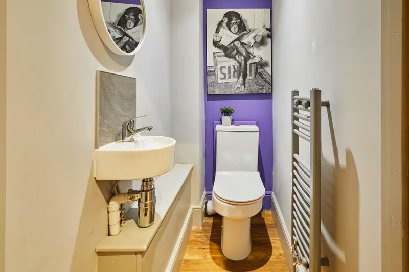 Compact bathroom with wall-mounted sink, toilet, towel rail and framed wall art