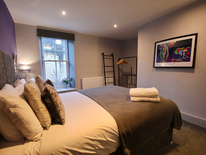 Bedroom with double bed, gold cushions, window, ladder shelf and framed wall art