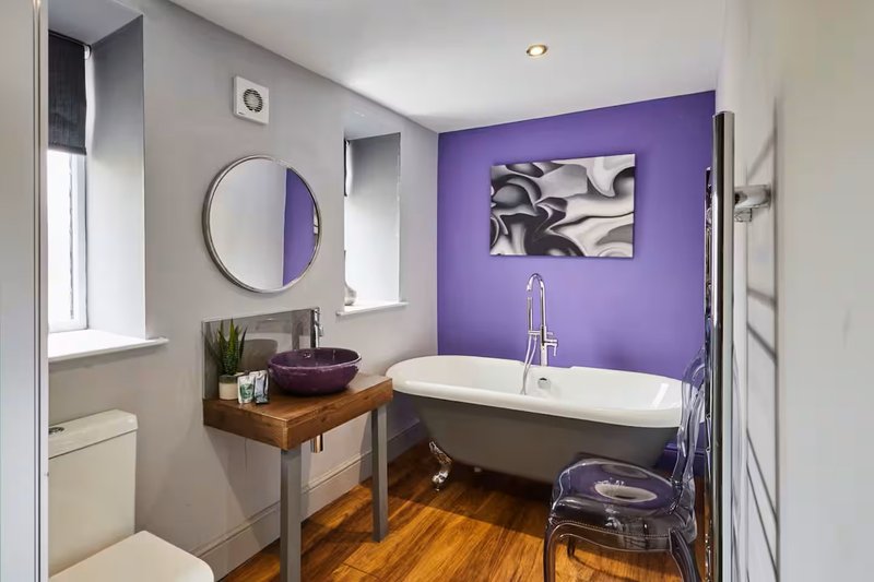 Modern bathroom with purple accent wall, freestanding bathtub, wooden vanity and circular mirror