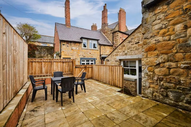 Stone cottage patio with dining table, chairs, and stone walls surrounding property