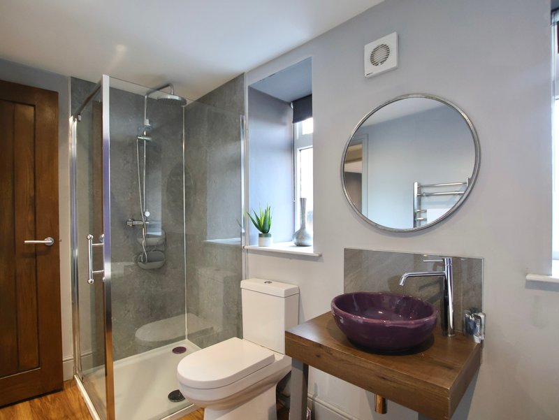 Modern bathroom with walk-in shower, toilet, burgundy vessel sink and round mirror