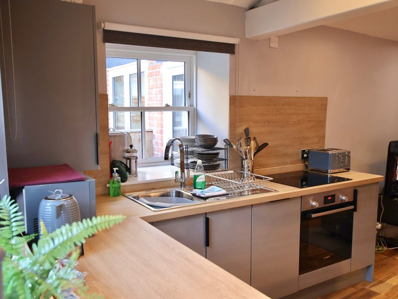 Modern kitchen with grey cabinetry, wooden countertop, sink, built-in oven and large window overlooking city