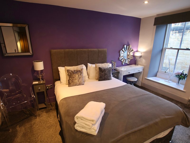Modern bedroom with purple accent wall, double bed, bedside lamps and large window