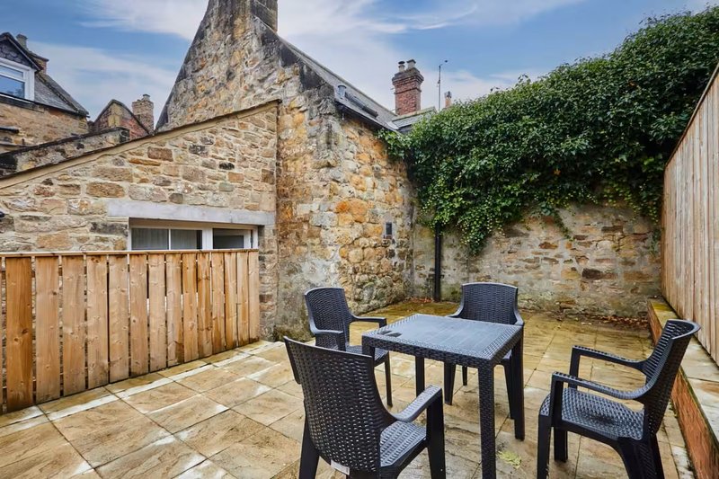 Stone cottage courtyard with outdoor dining table, chairs, and ivy-covered walls