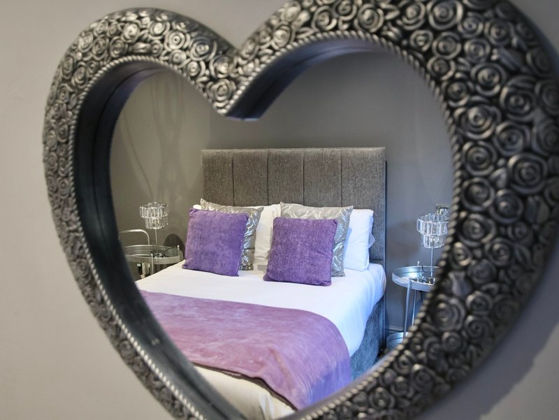 Bedroom with double bed, purple bedding, and decorative heart-shaped mirror on wall