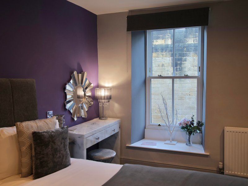 Bedroom with purple accent wall, dressing table, decorative mirror and large window overlooking city