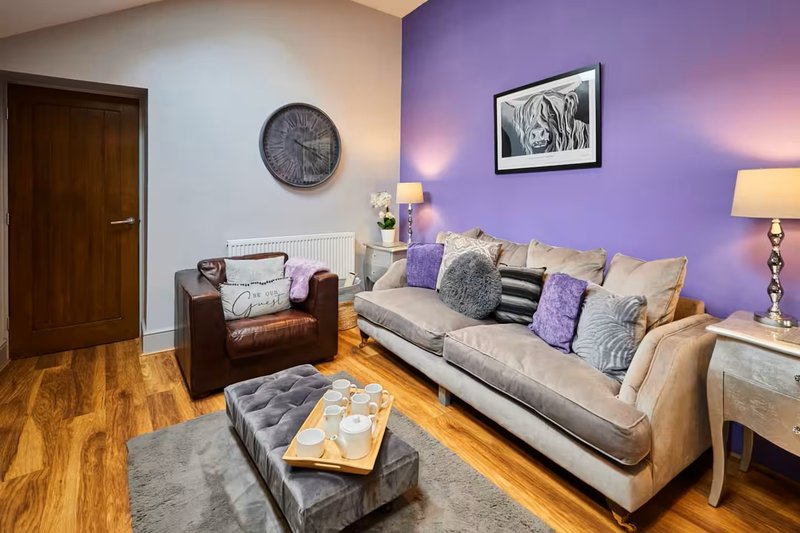 Living room with beige sofa, purple accent wall, brown armchair, and wooden floor