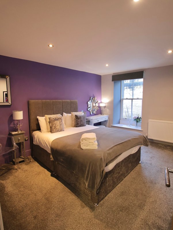 Bedroom with purple accent wall, double bed, bedside lamps, and window seat area
