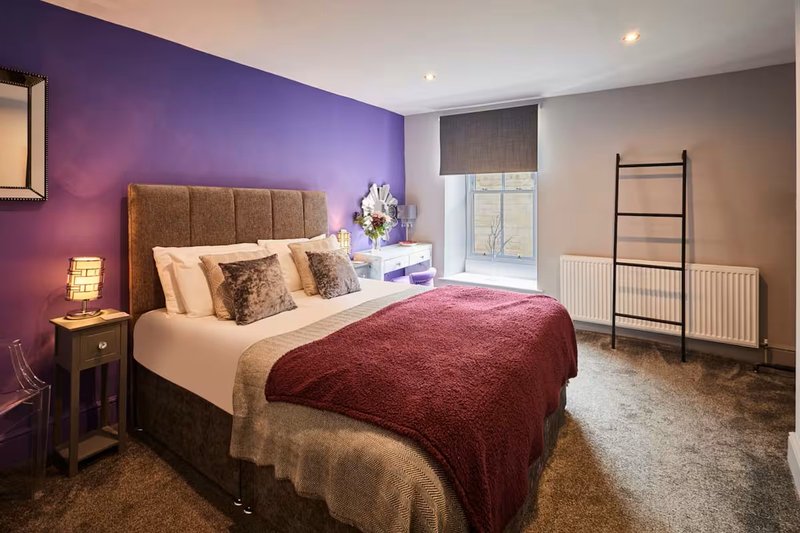 Modern bedroom with purple accent wall, double bed, bedside lamp and radiator