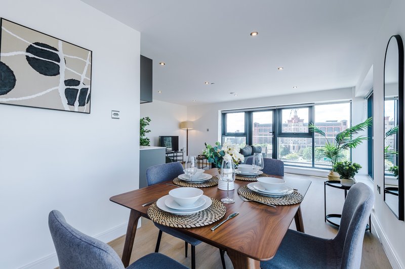 Modern dining area with wooden table, place settings, and floor-to-ceiling windows overlooking cityscape