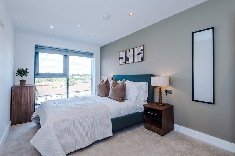 Bright modern bedroom with double bed, teal headboard, wooden nightstands and balcony doors