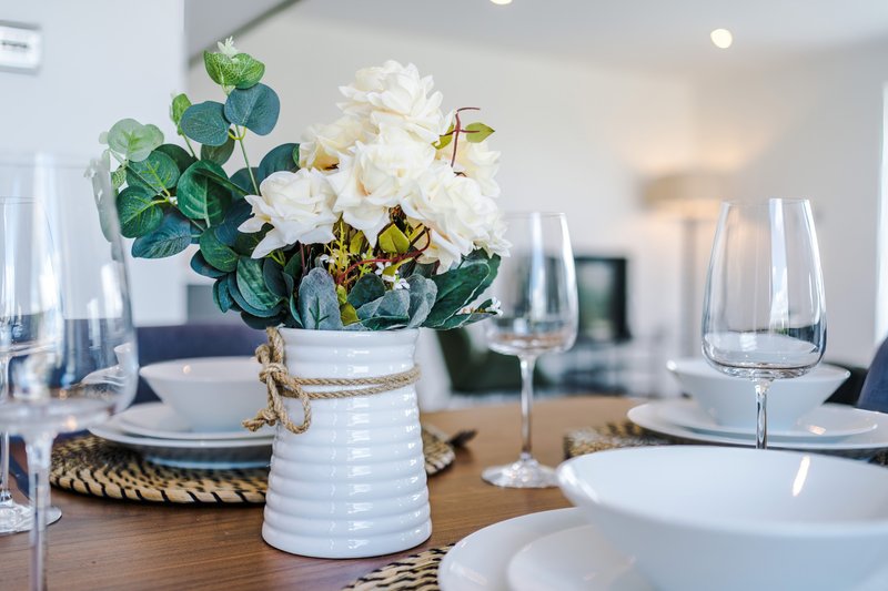 Dining table set with white flowers in vase, place settings and glassware