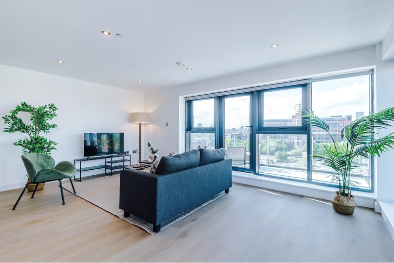 Modern living room with blue sofa, TV stand, potted plants and floor-to-ceiling windows overlooking city