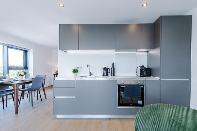 Modern kitchen with gray cabinetry, white countertop, built-in oven and dining area visible