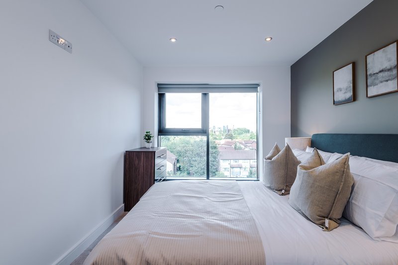 Modern bedroom with double bed, large window, teal headboard and neutral bedding