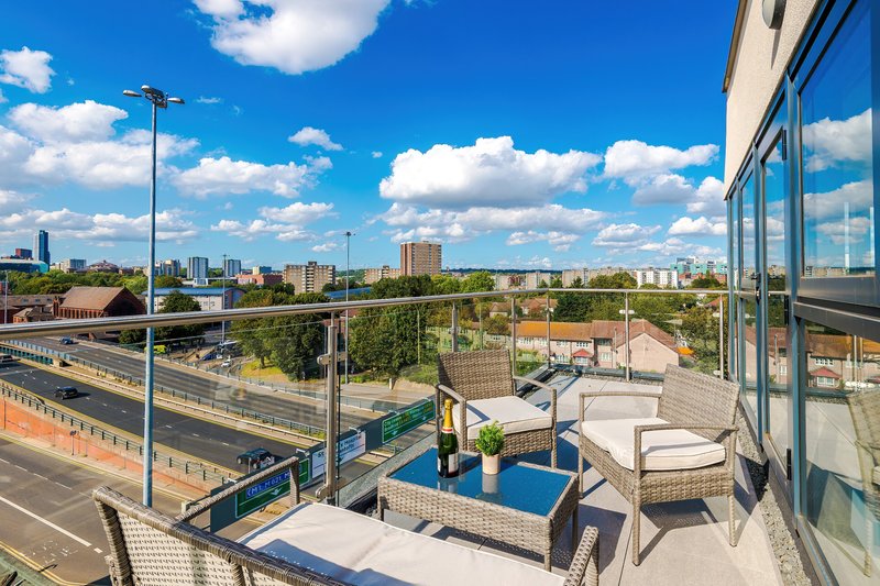 Modern balcony with wicker seating, blue cushions, city skyline view and blue sky