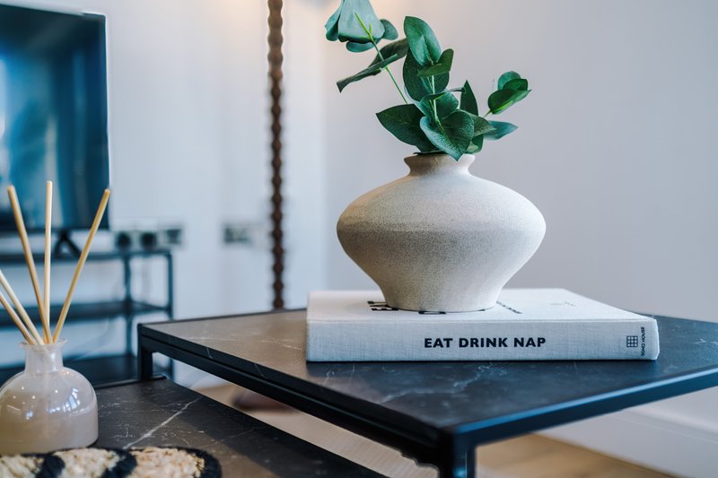 Modern side table with white ceramic vase, potted plant, decorative book, and reed diffuser