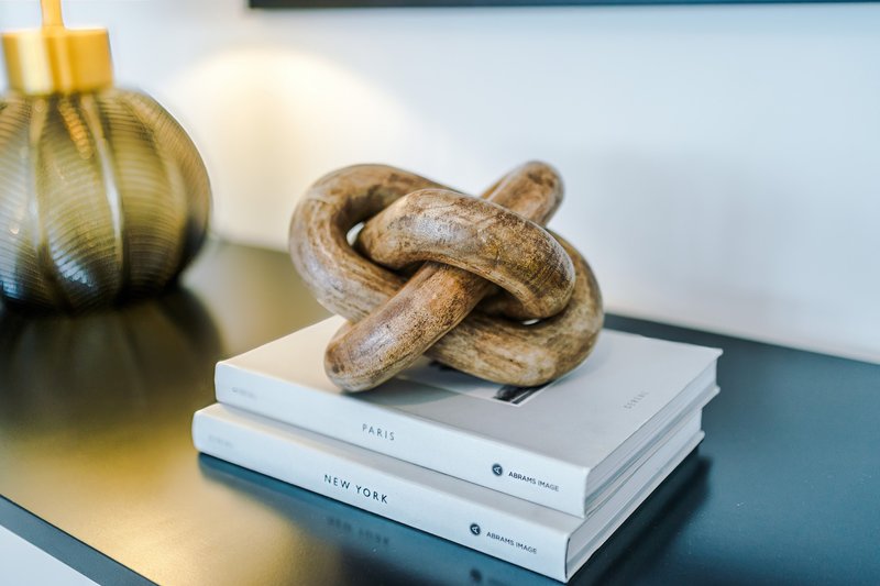 Decorative shelf with wooden knot sculpture, stacked books, and gold vase